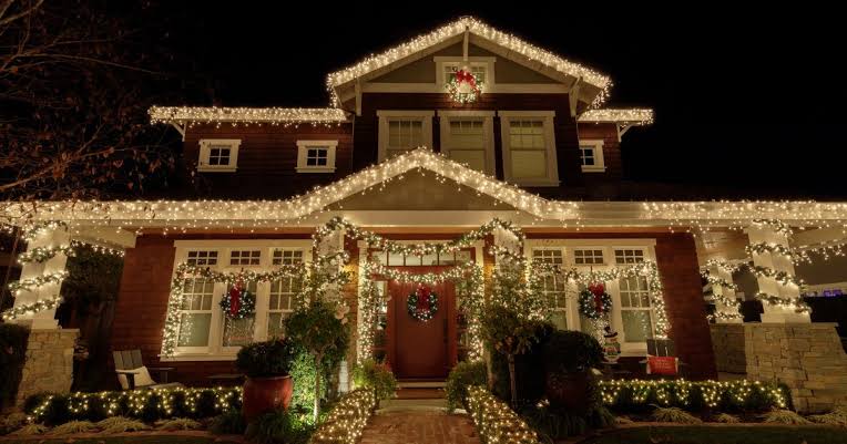 Warm-white icicle lighting and garland installed along a roofline, porch, and entryway for the Christmas season