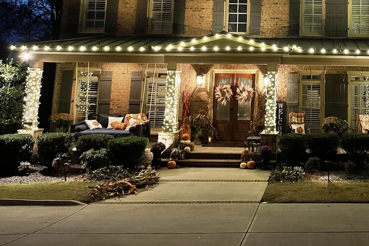 Light-wrapped porch columns and a lit roofline framing the front entry of a home at night