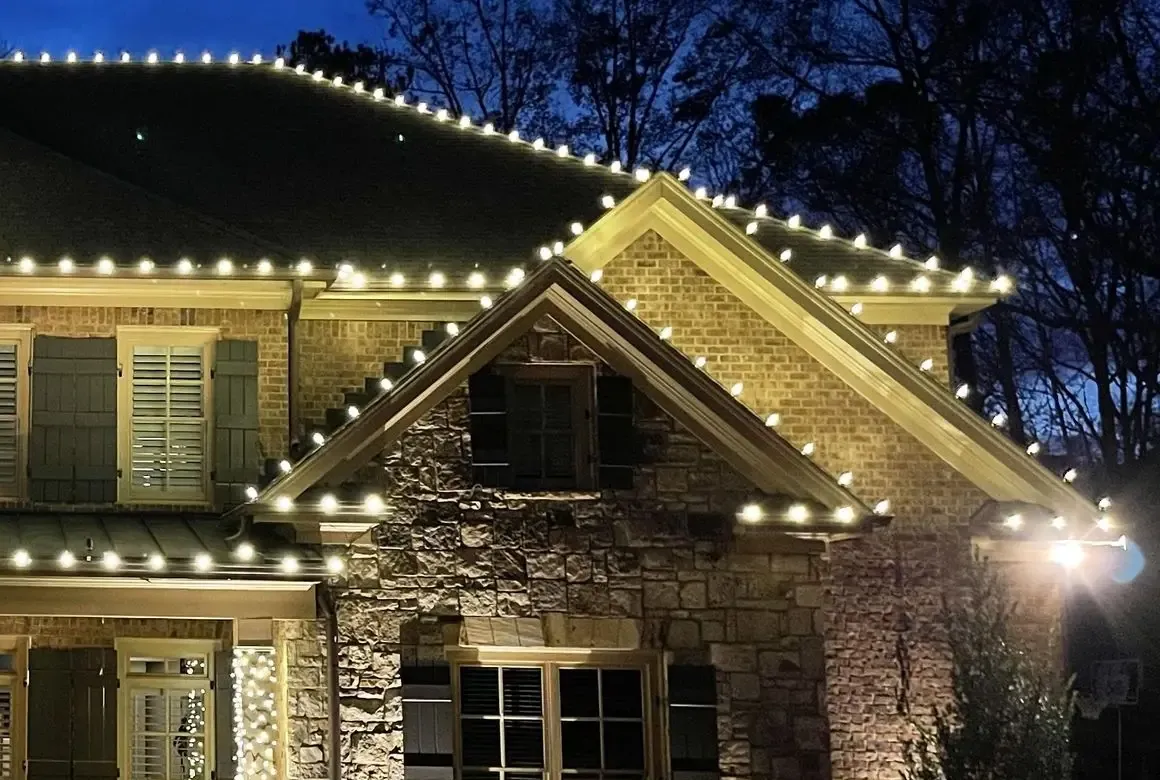 Warm-white Christmas lights tracing the roofline and gable peaks of a brick and stone home