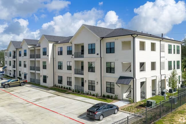 Modern apartment complex exterior with light-colored siding and a parking area