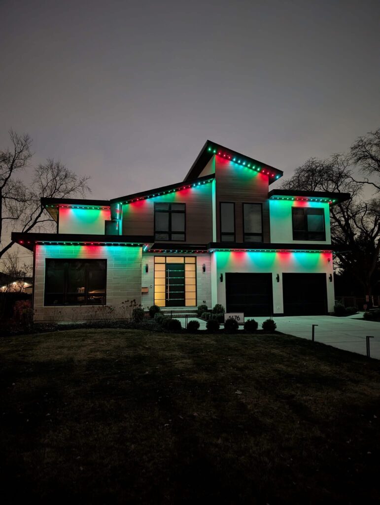 Permanent exterior LED lighting along the roofline of a modern home, shown in a red and green color pattern