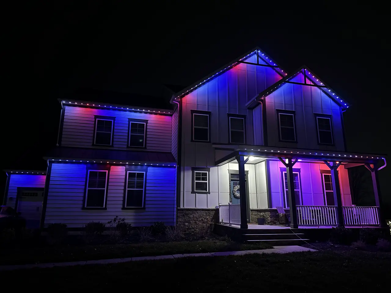Permanent exterior LED lighting on a home's roofline and covered porch, shown in a red and blue color-changing pattern
