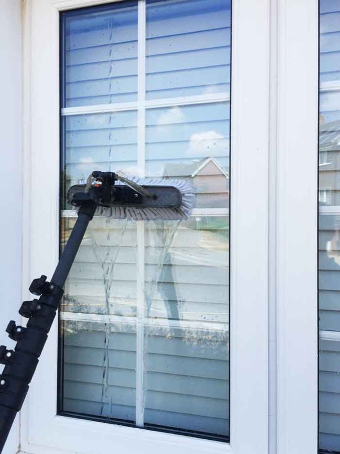 Technician using a water-fed pole to clean a second story window
