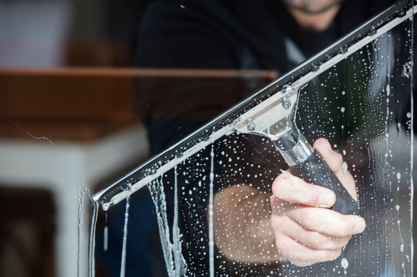 Close-up of a squeegee scrubbing a soapy window clean